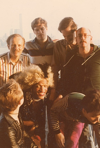 A Photograph of Marsha P. Johnson With Curly Blonde Hair, Leaning Forward Posing Outside with Friends