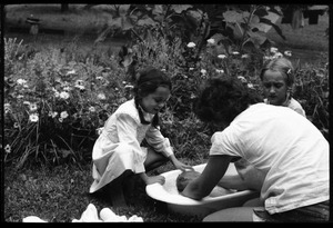 Nina Keller (back to camera), Sequoya Frey (right), and unidentified girl bathing an infant outdoors, Montague Farm Commune