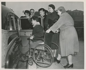 Red Cross volunteers help a man in a wheelchair into a car