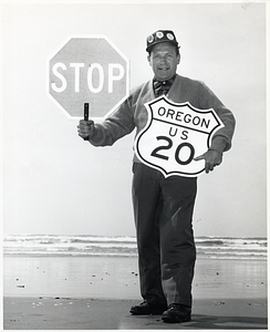 Unindentified man posing on a beach with a stop sign and sign for United States Route 20 in Oregon