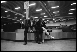 Stephen Stills (in heavy fur coat) and Judy Collins seated on an airport baggage carousel