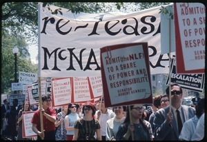 Anti-Vietnam War protesters marching with signs reading 'Admit (the NLF) to a share of power and responsibility' and 'Re-lease McNamara'