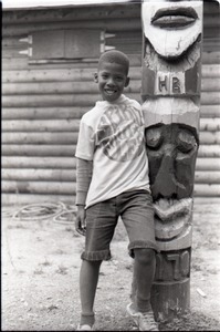African American boy in Spirit in Flesh t-shirt, posed next to "totem pole" at summer camp