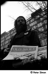 Bearded man selling the Old Mole outside the Cambridge Trust Co.