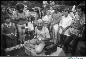 Ram Dass seated on a small platform during his appearance at Andrews Amphitheater, University of Hawaii, surrounded by a small group