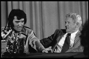 Elvis Presley answering questions at his press conference, with father Vernon Presley at the table with him (right)