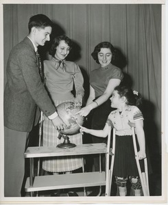 Four disabled young people pointing out their home countries on a globe