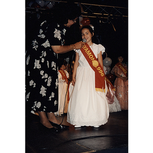 A girl wearing a Bayamon sash speaks into a microphone at the Festival Puertorriqueño