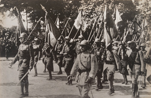 Street-level view of French soldiers marching with battle flags