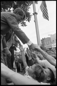 Robert F. Kennedy atop an outdoor stage, shaking hands with the crowd at the Turkey Day parade while stumping for Democratic candidates in the northern Midwest