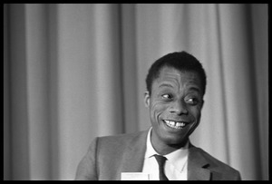 James Baldwin, smiling, while sitting on a panel at the Youth, Non-Violence, and Social Change conference, Howard University