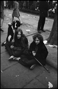 Three young women sit on the sidewalk, observing the Moratorium protests