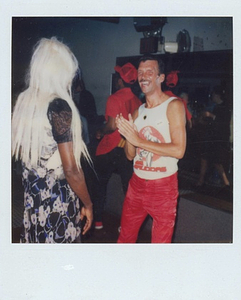 A Photograph of Marsha P. Johnson with Long Blonde Hair and Wearing a Black and Pink Patterned Dress From Behind