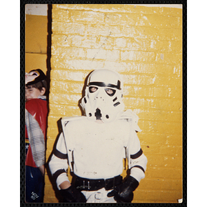 A child poses in a Halloween costume in front of a yellow brick wall