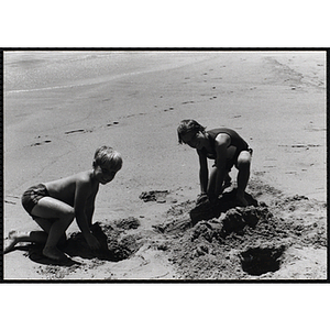 Two boys dig holes in the sand at the shoreline on a beach