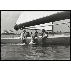 A teenage girls hangs off the side of sailboat held by another girl as three other teenagers look on in Boston Harbor