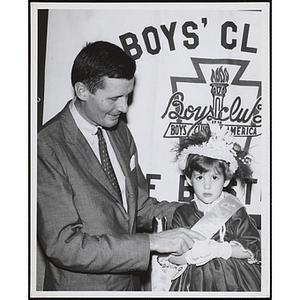 A man adorns Miss Bunker Hill with her sash at a Boys' Club Little Sister Contest