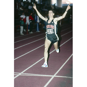 A Northeastern student, number 319, from the men's indoor track and field team crossing the finishing line at the Greater Boston Championships at Harvard