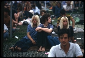 Three women seated on a fallen chain link fence at the Woodstock Festival