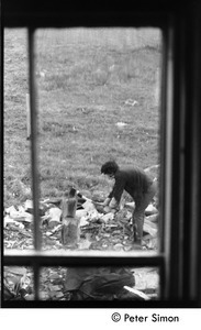 Steve Marsden chopping wood, viewed through a window, Montague Farm Commune