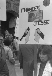 Protester holding sign reading 'Frances - Jesse' with images of Frances Crowe kissing Jesse Jackson, a peace symbol, and cartoon of a gun being broken