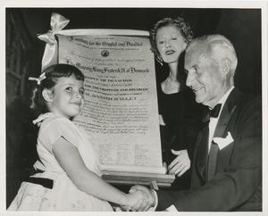 Young girl shaking hands with older man in front of a proclamation thanking King Frederik IX of Denmark