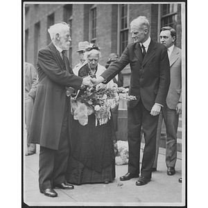 Two men hold hands at George Meserve Tribute in front of woman holding a bouquet of flowers