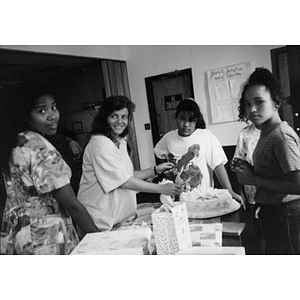 Women preparing to cut a cake during an office celebration.