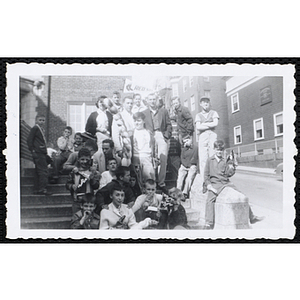 Several men and women posing with about twenty boys on the stairs outside the Charlestown Boys' Club building, some of them holding "BU Service Day" pennants and a Boston Red Sox pennant