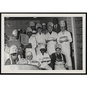 Members of the Tom Pappas Chefs' Club hold decorated cakes and pose with an unidentified man in a kitchen
