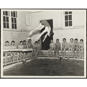 A boy performs a dive in a natatorium pool as a group of boys look on