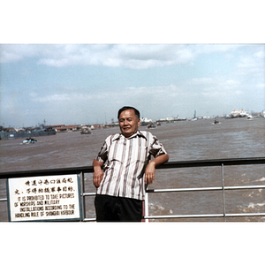 Male Association member leans against a railing in front of Shanghai Harbor