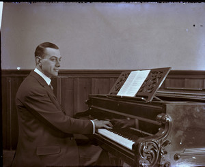 Three-quarter portrait of a man, seated at a Chickering piano, facing right, location unknown.