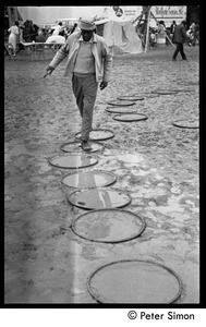 Man walking across muddy ground, using oil drum lids as stepping stones, Resurrection City encampment