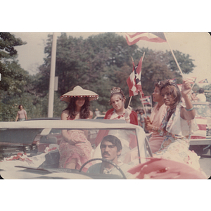 Four women sit on the back of a car during a parade for the Festival Puertorriqueño