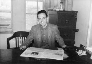 Suffolk University student Bud O'Brien, sports editor for the Suffolk Journal, seated at desk, 1958