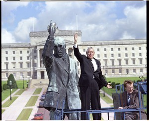 Rev. Ian Paisley posing beside the statue of Sir Eward Carson in front of the Stormont building, standing on a 40 ft. high hydraulic lift