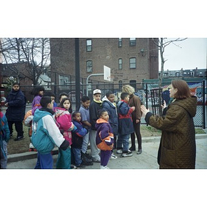 Teacher addressing a group of children outside.