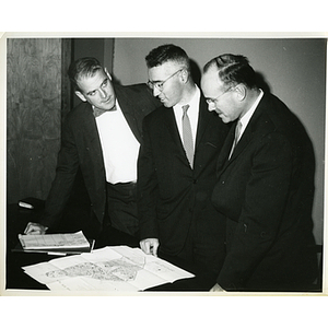 Thomas E. Leggat, standing in the middle, examines an illustrative site plan with two unidentified men