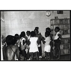 A group of girls standing in a circle and clapping each other's hands, while others look on, in a swimming pool locker room
