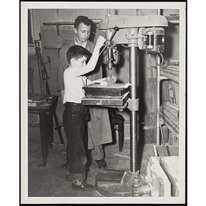 A young man and a boy from the Boys' Clubs of Boston using a drill press for a woodworking project