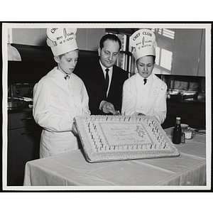 Two members of the Tom Pappas Chefs' Club and Mr. Cerrone pose with cake decorated with the message "Mothers' Club on our 70th Anniversary Boys Clubs of Boston"