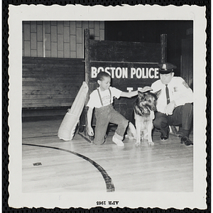 A boy pets a police dog as a Boston Police officer looks on during a K-9 demonstration in a gymnasium