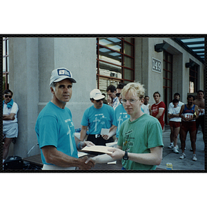 A man receives a certificate from another man as they shake hands at the Battle of Bunker Hill Road Race