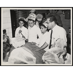 Members of the Tom Pappas Chefs' Club stand around a work table with Brandeis University's Director of Dining Halls and Chefs' Club Committee member Norman R. Grimm in a Brandeis University kitchen