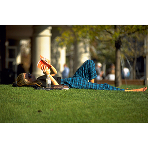 Student lying on the grass in Centennial Common while she holds a book above her to read