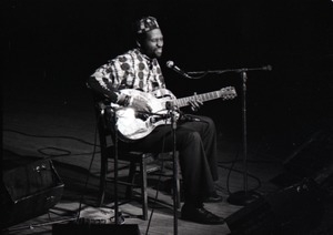 Taj Mahal in concert at Northfield, Mass.: Taj Mahal seated, playing steel guitar