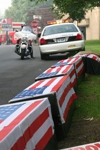 Fake caskets draped in American flags lining the road, with sign reading 'Out of Iraq'