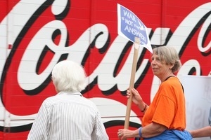 Anti-Iraq War protester with sign reading 'War is not the answer,' with huge Coca Cola sign in the background