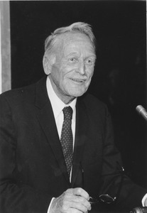 Frederick Troy holding eyeglasses in front of a microphone